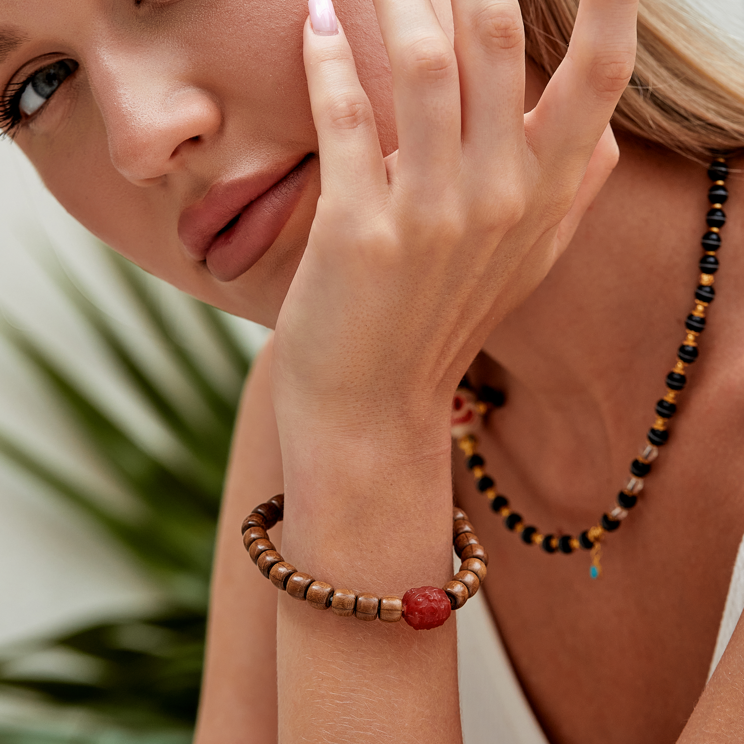 Woman wearing a beaded sandalwood bracelet and amber beaded necklace with a blurred green background - Zodori Studio